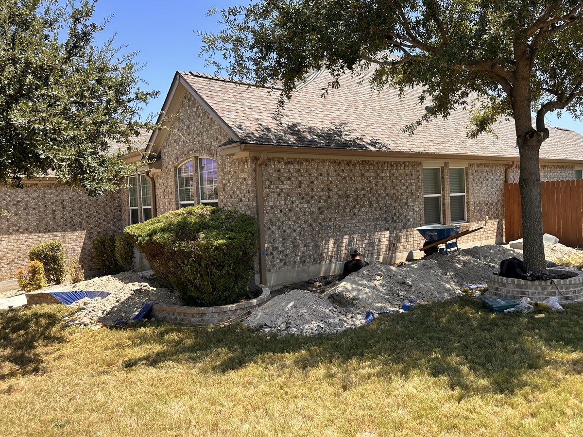 Spoil piles along the front foundation beds of a brick home during pier installation